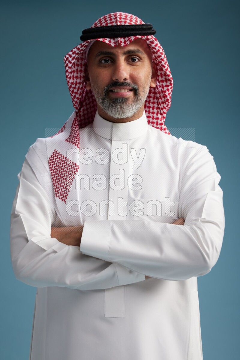 Saudi man wearing thob and shomagh posing to the camera on blue background