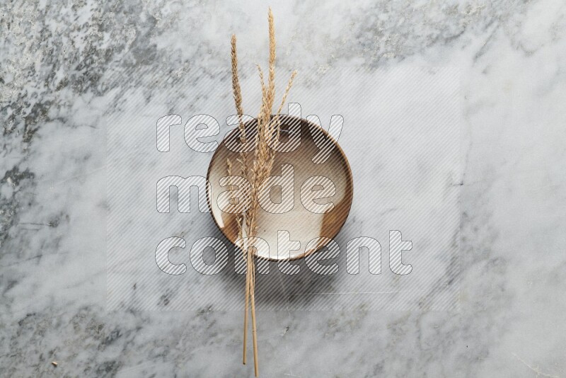 Wheat stalks on multicolored pottery plate on grey marble background