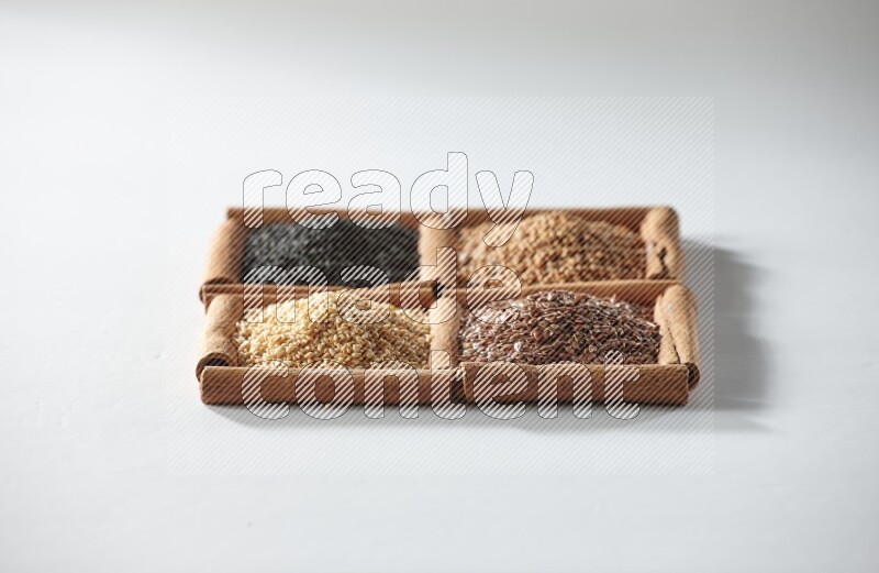 4 مربعات من أعواد القرفة ممتلئة بحبة البركة وبذور الخردل وبذور الكتان والسمسم على أرضية بيضاء