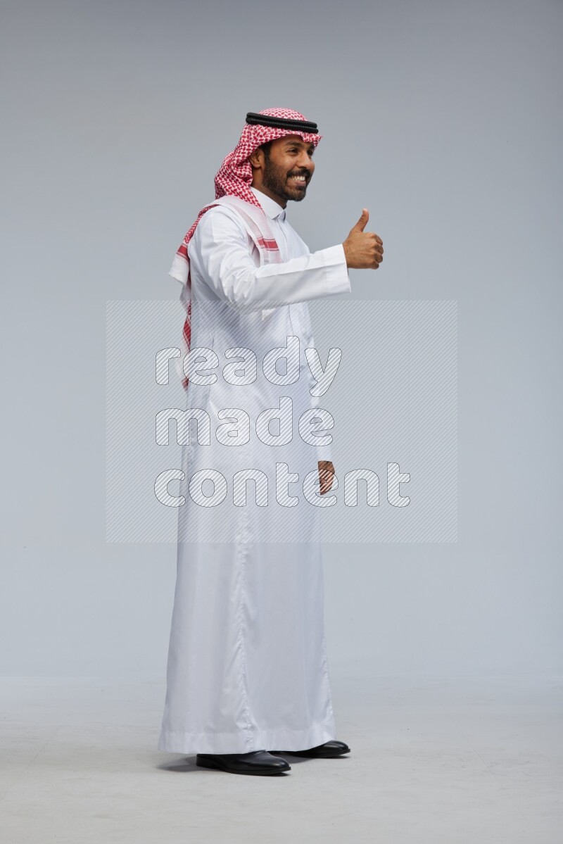 Saudi man Wearing Thob and shomag standing interacting with the camera on Gray background