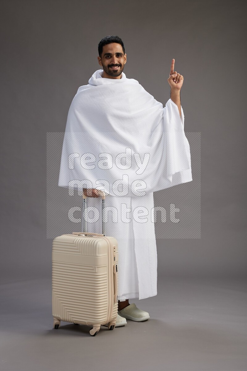 A man wearing Ehram Standing holding traveling bag on gray background