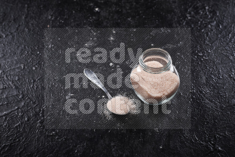 A glass jar full of fine himalayan salt on black background
