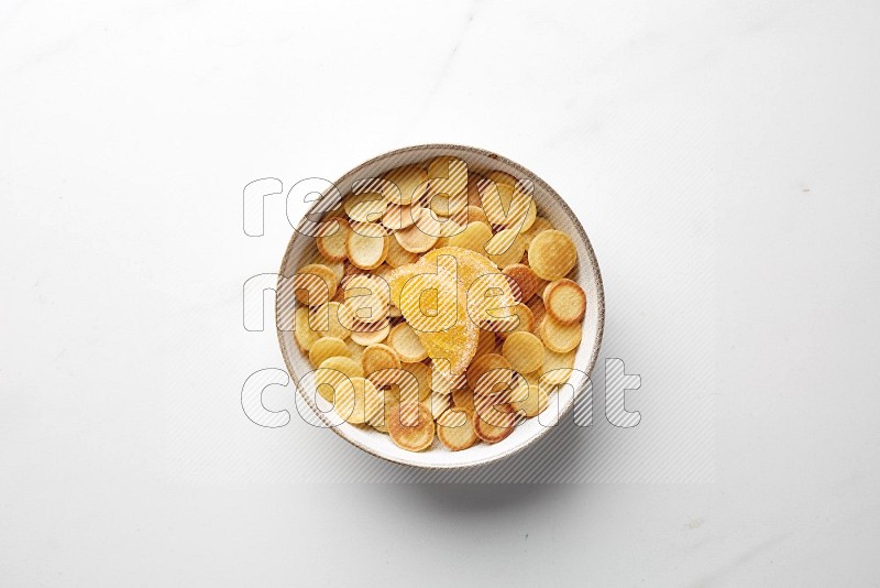Top-view shot of orange candy cereal pancakes in a round bowl on white background