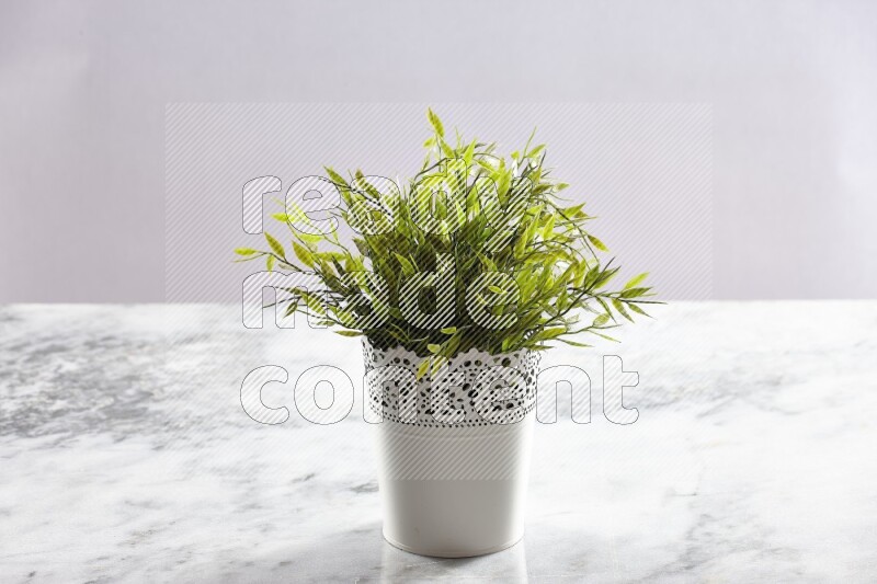Green artificial plant in white decorative pot on grey marble background