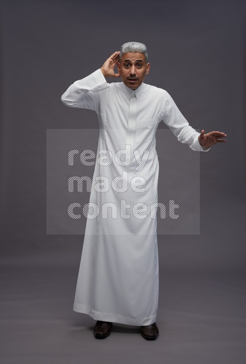 Saudi man wearing thob standing interacting with the camera on gray background
