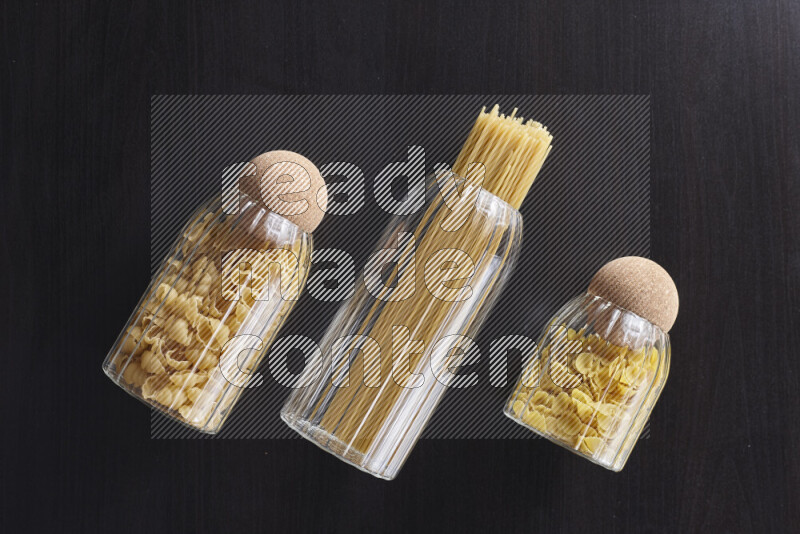Raw pasta in glass jars on black background