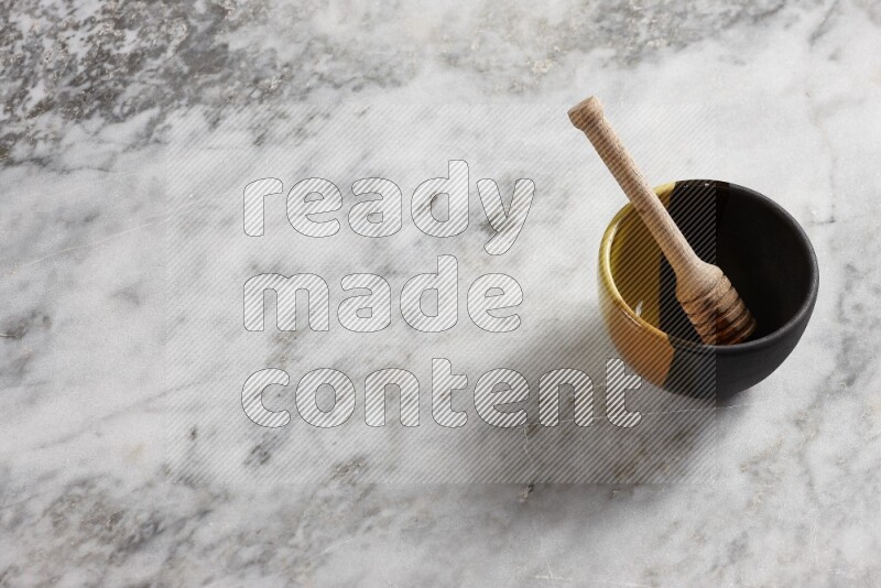 Multicolored pottery bowl with wooden honey dipper in it on grey marble background