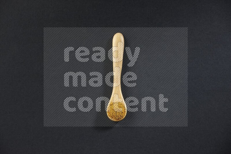 A wooden spoon full of turmeric powder on black flooring