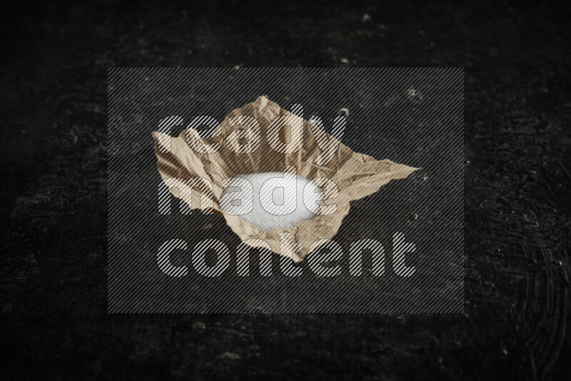 A crumpled piece of paper full of white salt on black background
