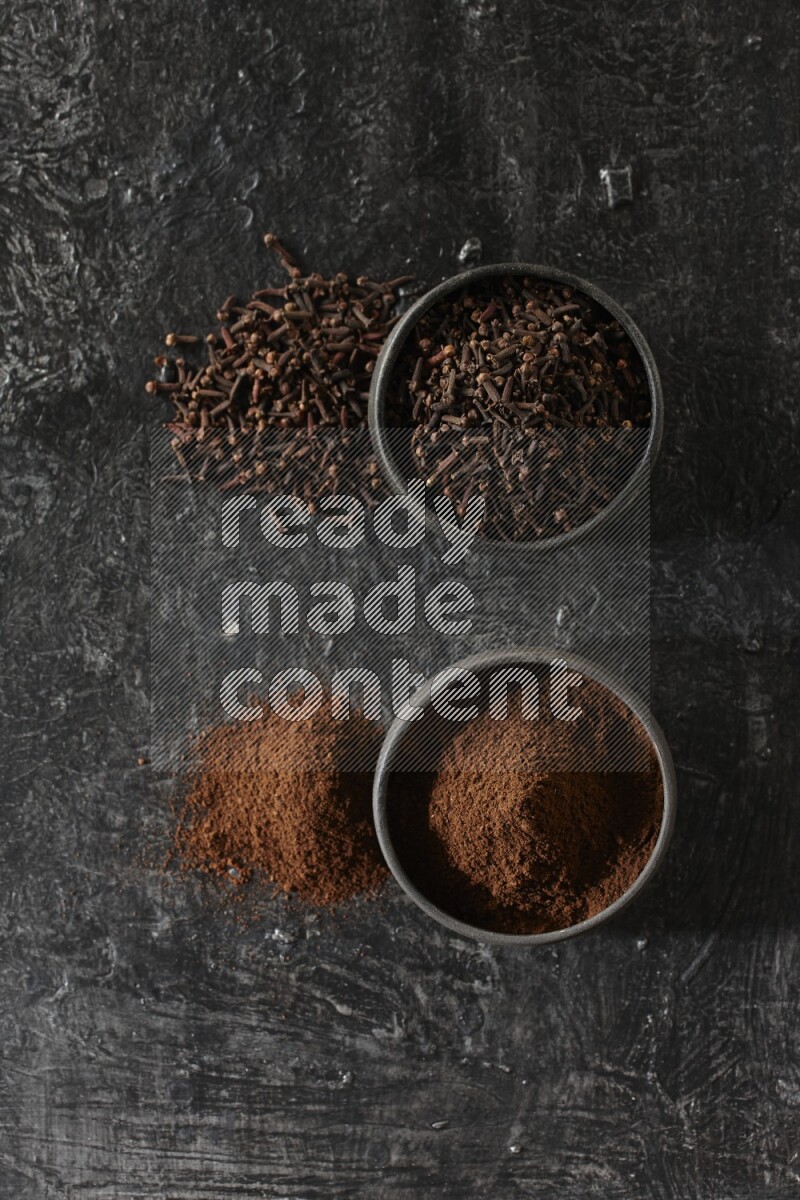 وعاءين من الفخار الأسود أحدهما ممتلئي بحبوب القرنفل والآخر ممتلئ ببودرة القرنفل على خلفية سوداء