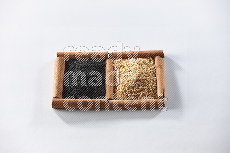 مربعان من أعواد القرفة ممتلئان ببذور السمسم وحبة البركة السوداء علي خلفية بيضاء