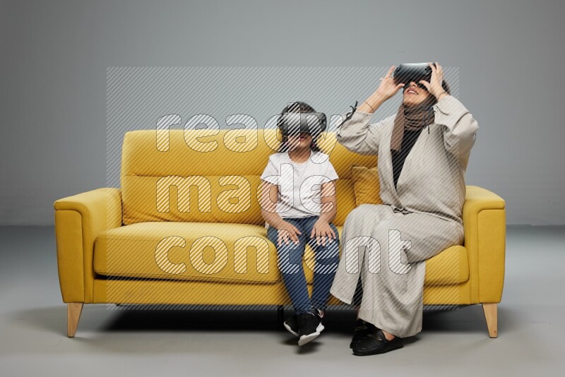 A girl and her mother sitting playing with VR on gray background