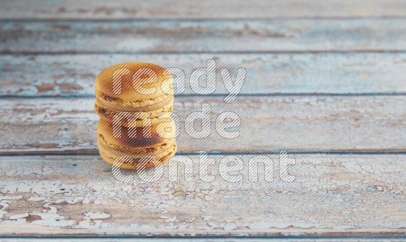 45º Shot of two Yellow Crème Brulée macarons on light blue wooden background