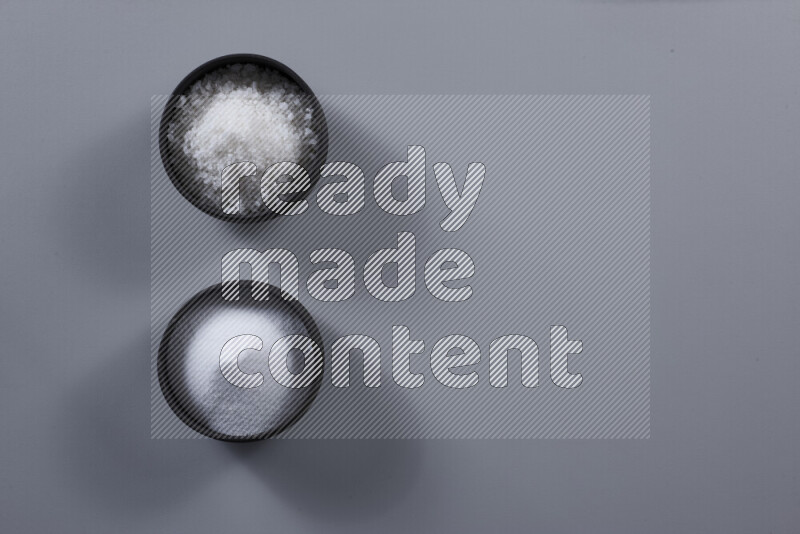 2 وعاء فخاري احدهمها ممتلئ بملح الطعام الأبيض والأخر بملح البحر الخشن على خلفية رمادية