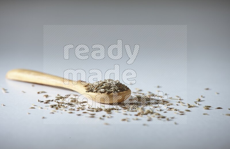 A wooden spoon full of cumin seeds on a white flooring