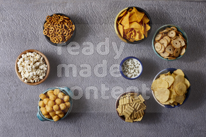 Assorted snacks in pottery bowls on grey background