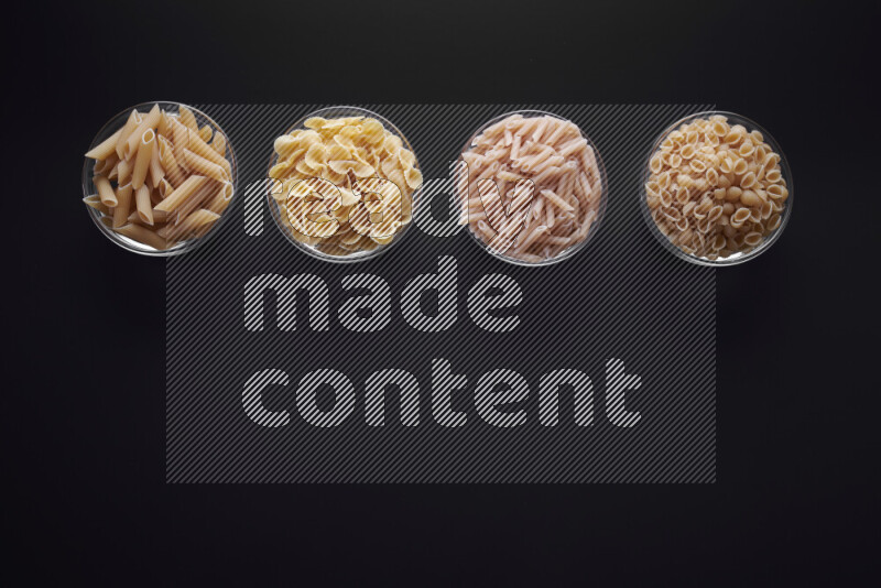Different pasta types in glass bowls on black background
