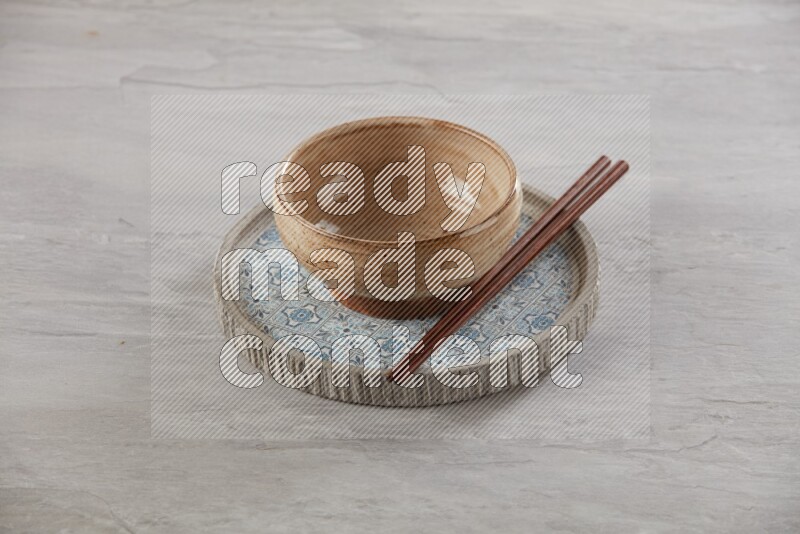 multi color pottery round bowl on top of multi color round ceramic plate and chopsticks, on grey textured countertop