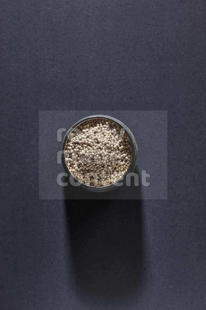 وعاء فخار أسود مملوء بالفلفل الأبيض على أرضية سوداء