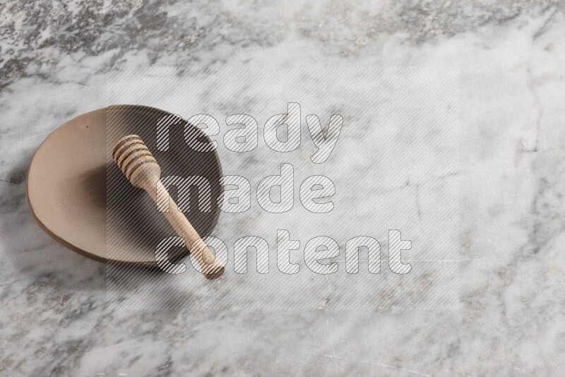 Multicolored pottery plate with wooden honey dipper in it on grey marble background
