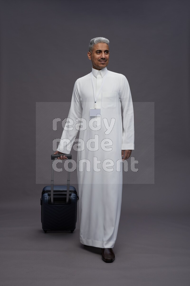 Saudi man wearing thob with neck strap employee badge standing holding bag on gray background