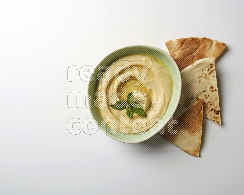 Hummus in a green plate garnished with mint on a white background