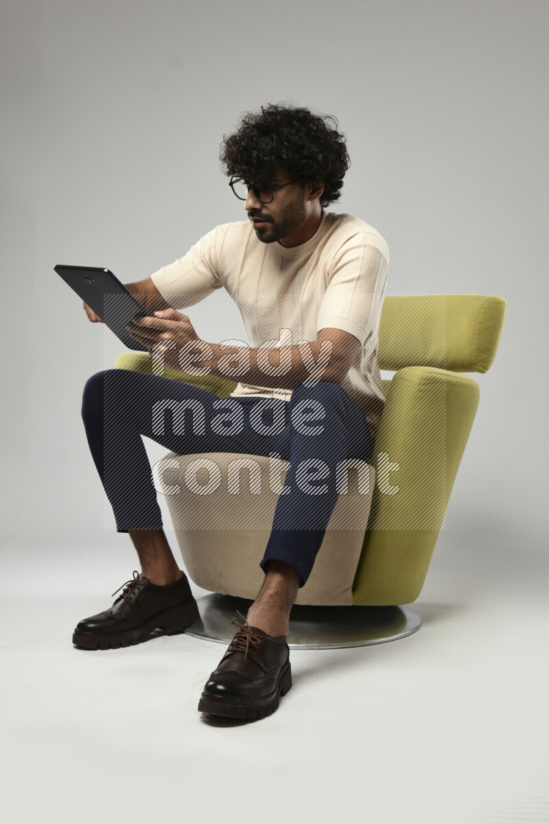 A man wearing casual sitting on a chair browsing on a tablet on white background