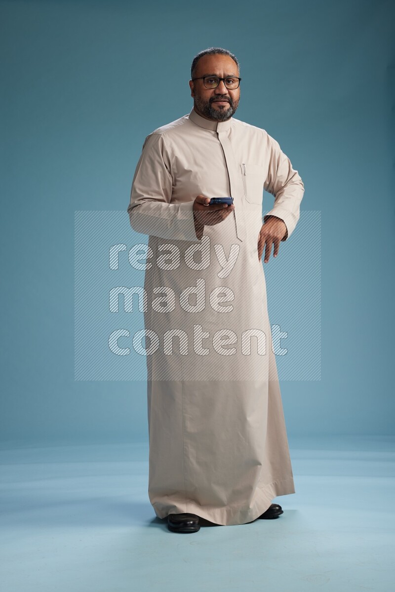 Saudi Man without shimag Standing texting on phone on blue background