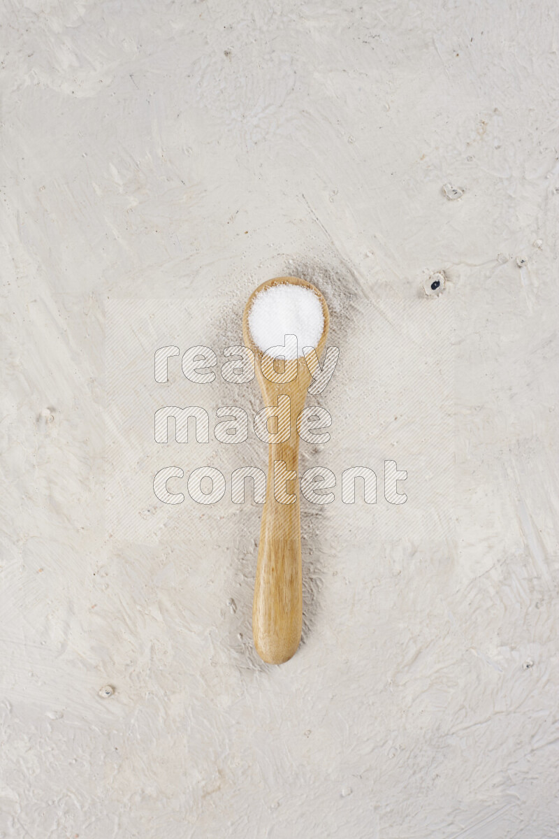 A wooden spoon full of white salt on white background