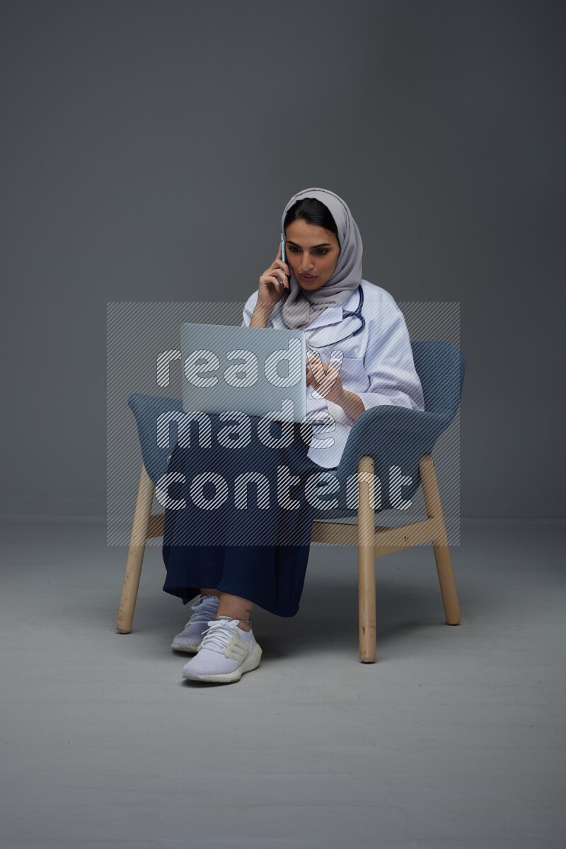 A doctor wearing a light gray head scarf sitting on blue chair on grey background