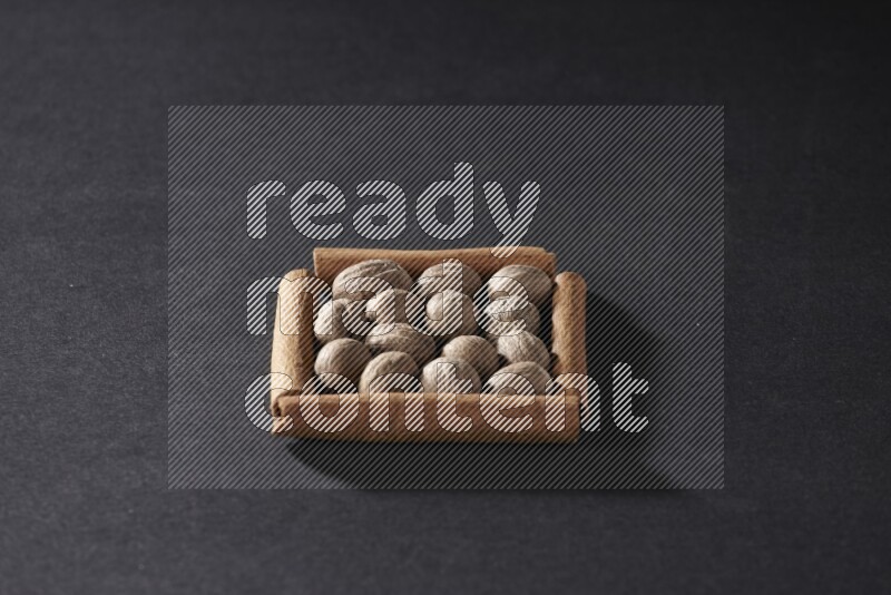 أربعة من أعواد القرفة مكونة شكل مربع بداخلها جوزة الطيب علي خلفية سوداء