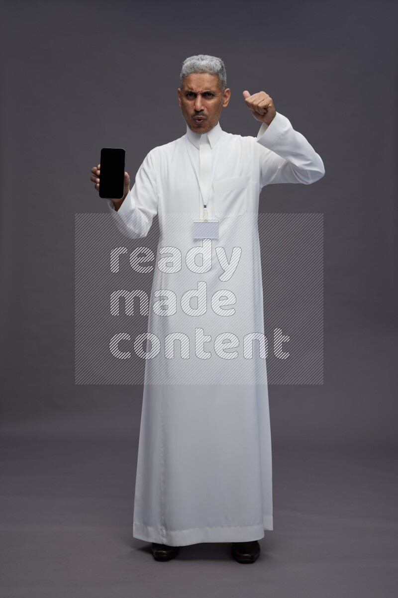 Saudi man wearing thob with neck strap employee badge standing showing phone to camera on gray background