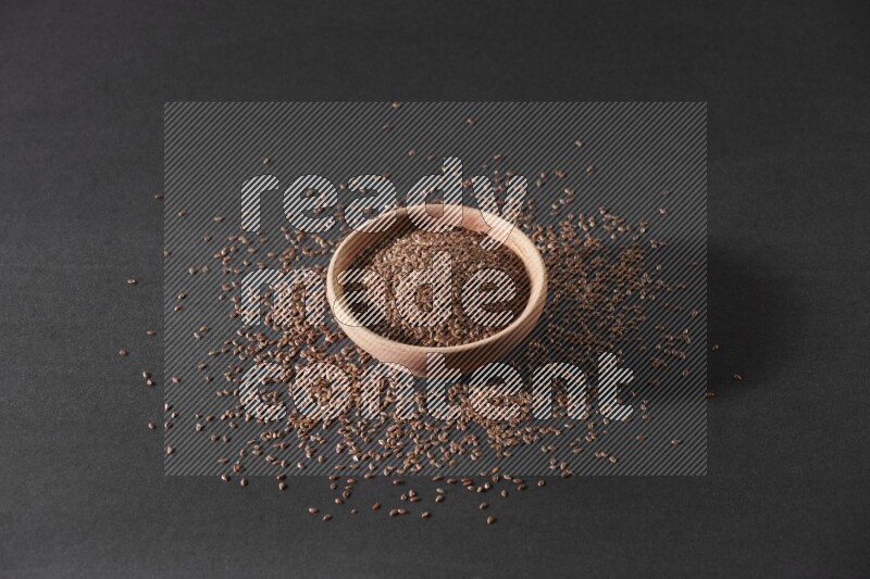 A wooden bowl full of flax surrounded by the seeds on a black flooring in different angles