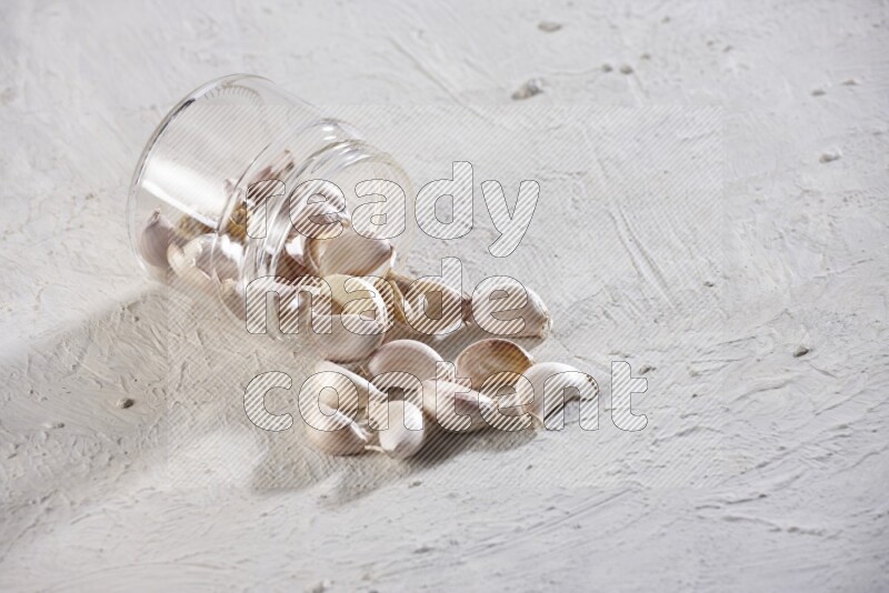 A glass jar full of garlic cloves flipped and the cloves came out on a textured white flooring