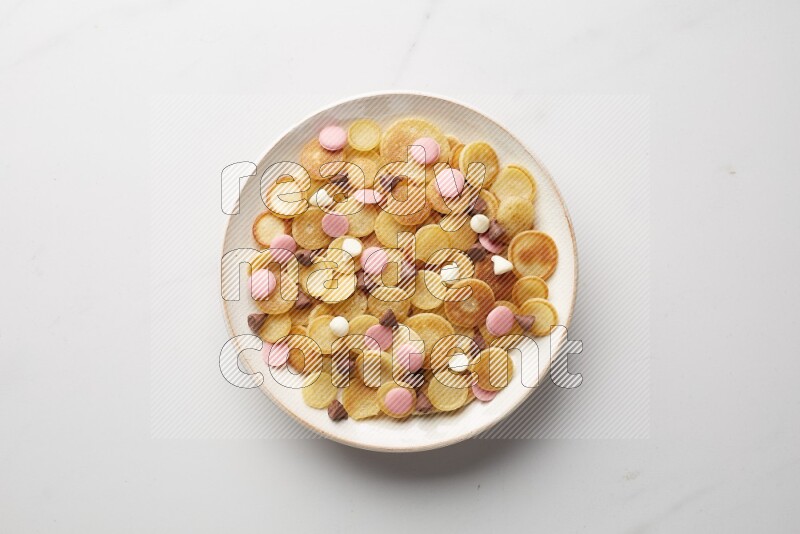 Top-view shot of mixed chocolate chips cereal pancakes in a round bowl on white background