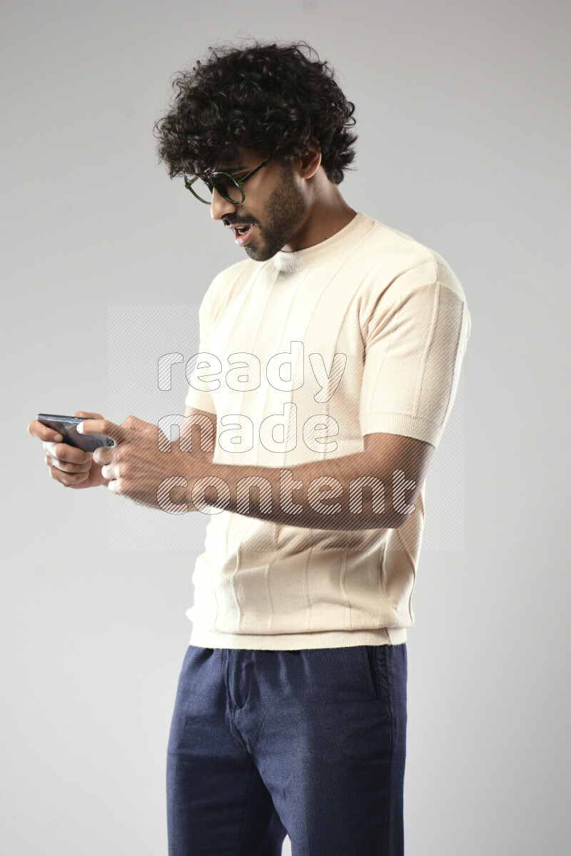 A man wearing casual standing and gaming on the phone on white background