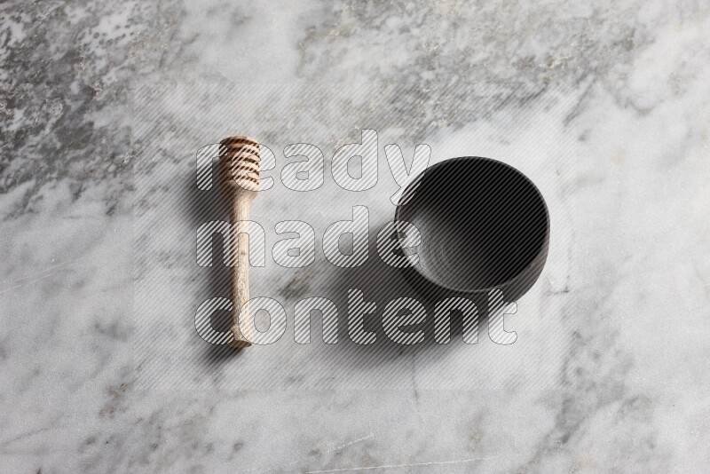 Black pottery bowl with wooden honey dipper on the side on grey marble background