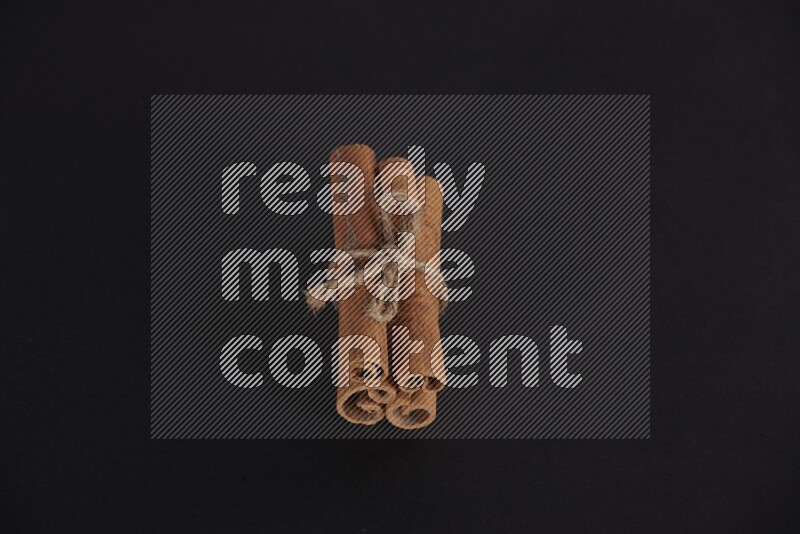 4 Cinnamon sticks stacked and bounded on black flooring