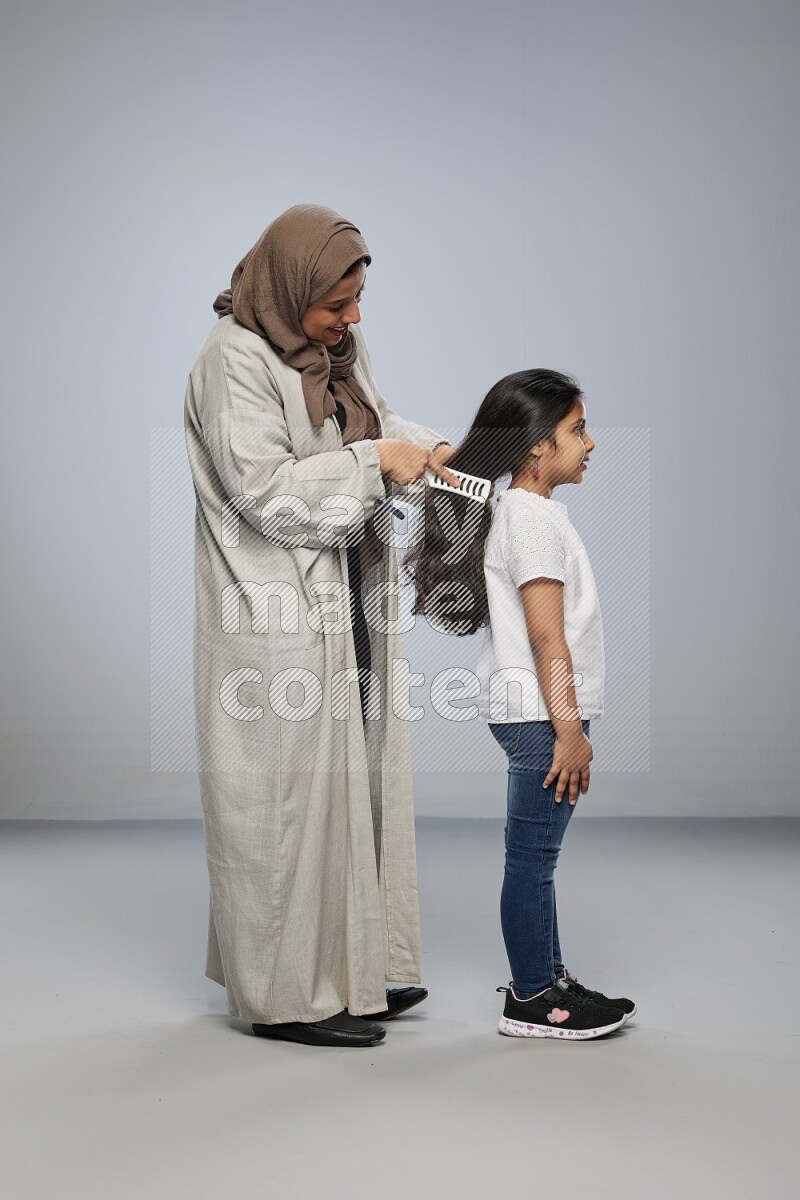 Mom standing styling hair for her daughter on gray background