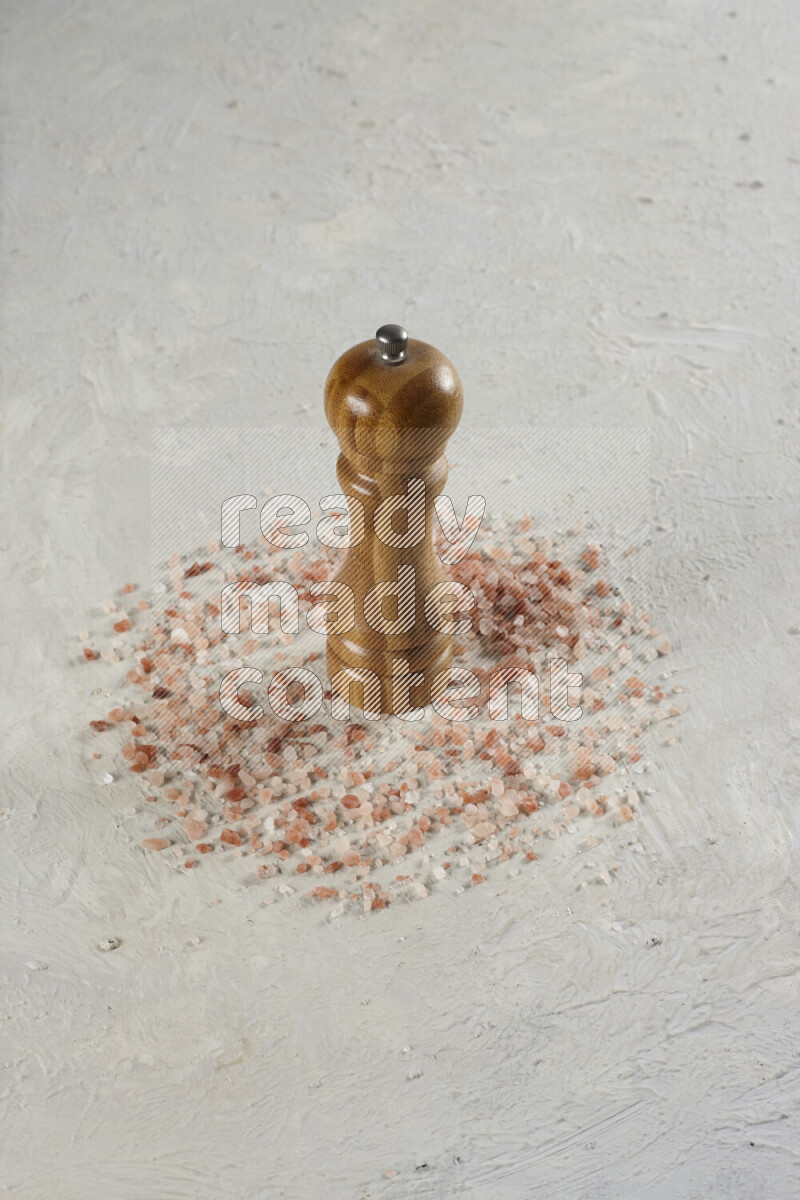 A wooden grinder standing upright and surrounded by coarse pink himalayan salt on white background