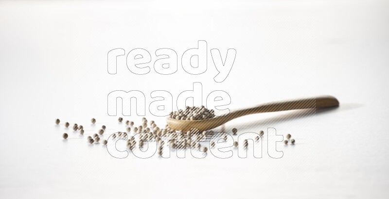 A wooden spoon full of white pepper beads on white flooring