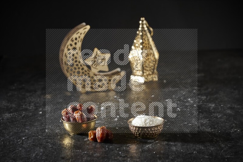Dates in a metal bowl with desiccated coconuts beside golden lanterns in a dark setup