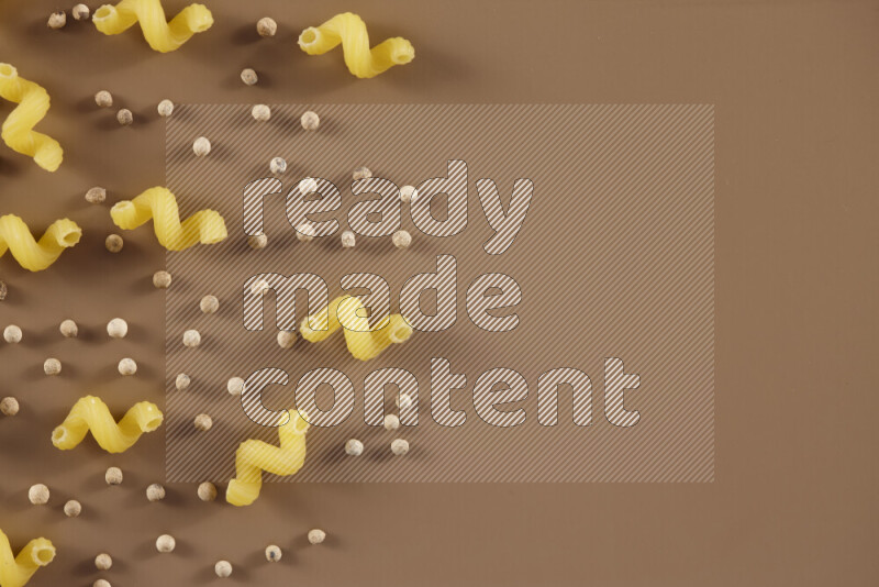 Raw pasta with different ingredients such as cherry tomatoes, garlic, onions, red chilis, black pepper, white pepper, bay laurel leaves, rosemary and cardamom on beige background