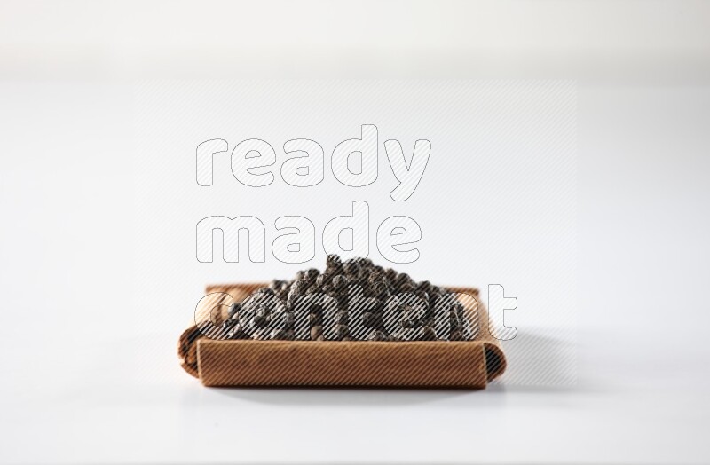 A single square of cinnamon sticks full of black pepper on white flooring
