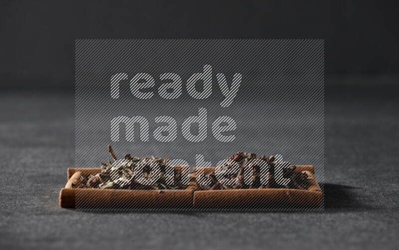 مربعان من أعواد القرفة ممتلئان بالقرنفل والريحان المجفف علي خلفية سوداء