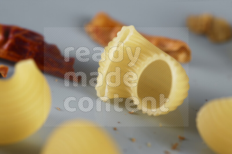 Raw pasta with different ingredients such as cherry tomatoes, garlic, onions, red chilis, black pepper, white pepper, bay laurel leaves, rosemary, cardamom and mushrooms on light blue background