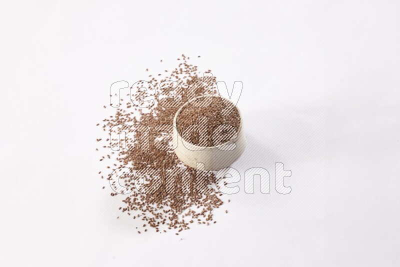 A pottery beige bowl full of flax seeds and more seeds spread on a white flooring