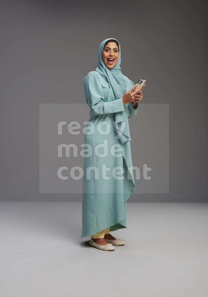 Saudi Woman wearing Abaya standing texting on phone on Gray background