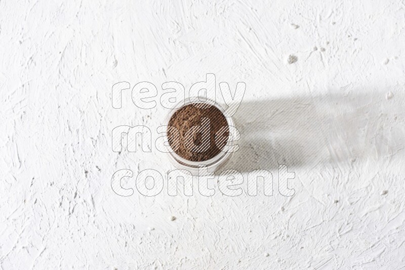 A glass jar full of cloves powder on a textured white flooring