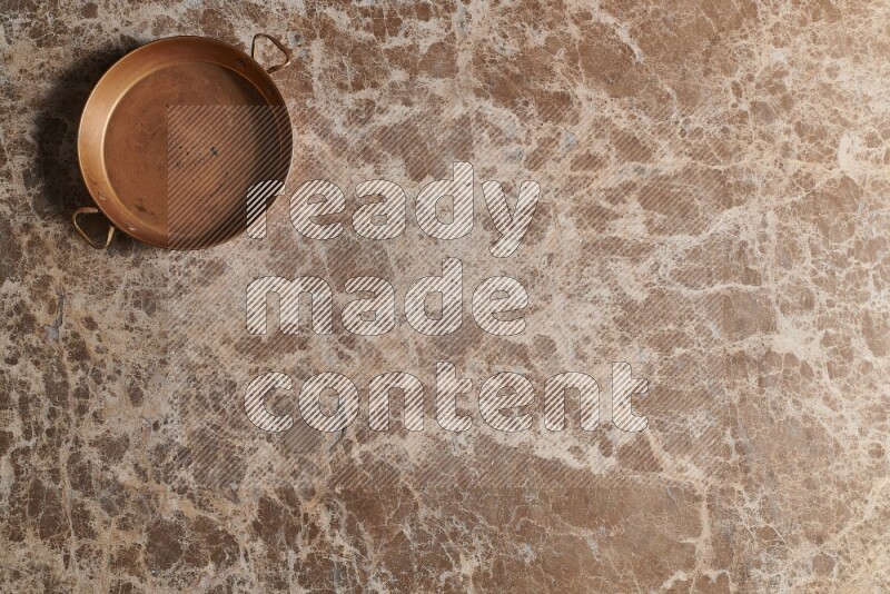 A small copper pan on beige marble background
